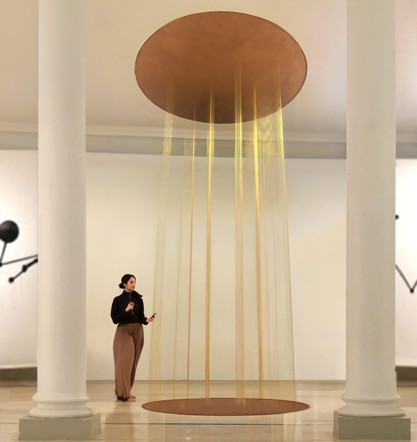 Installation suspendue de fils dorés sous un disque de cuivre, entre deux colonnes